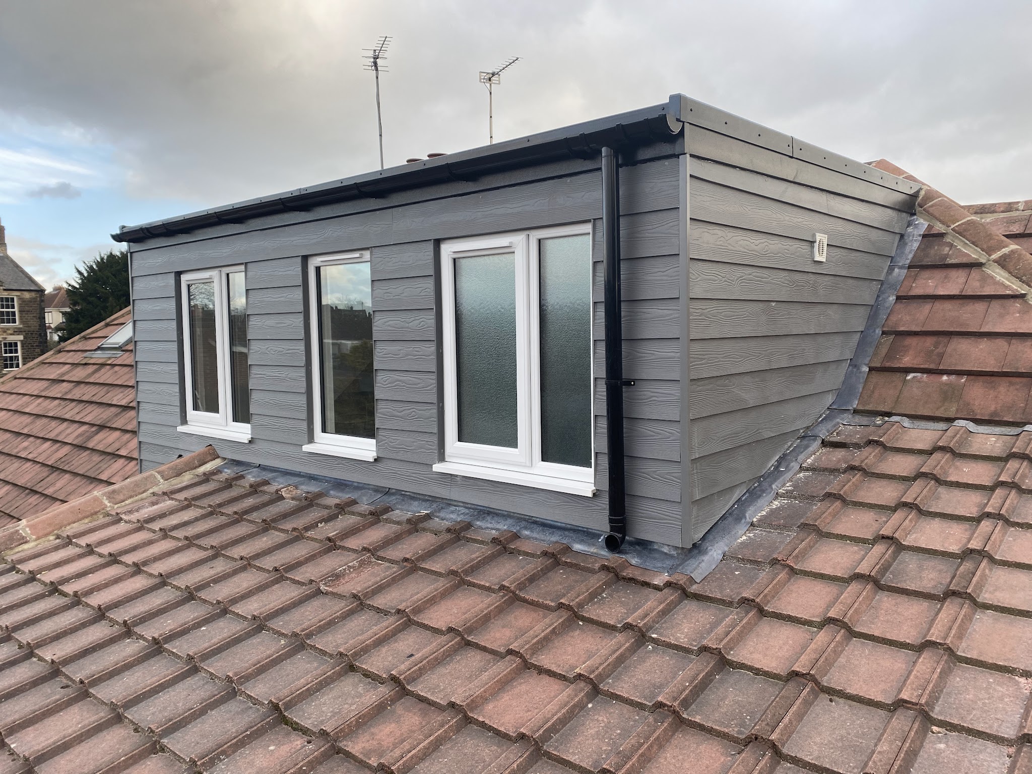 A grey-clad dormer extension with three windows on a tiled roof