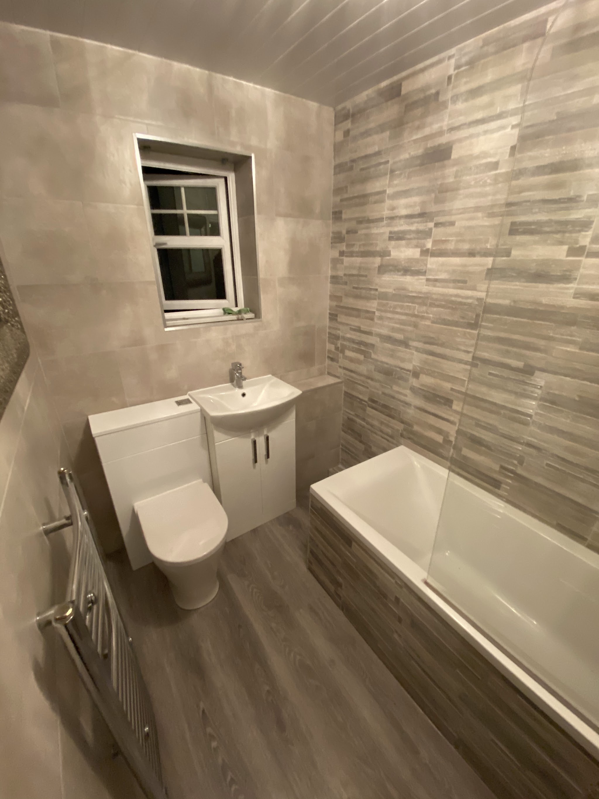 A refurbished bathroom with a bath and grey wall tiles